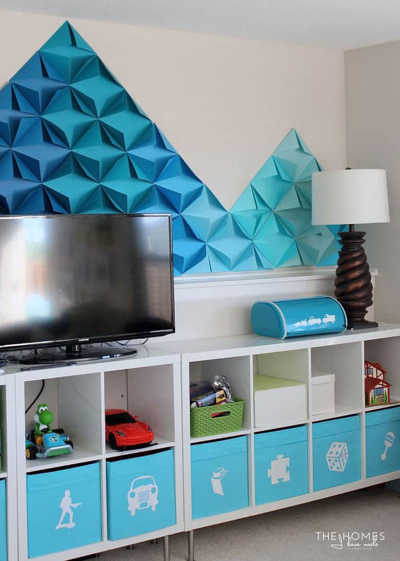 Brilliant blue triangle shaped origami paper design featured on playroom wall behind white console with matching blue accents.