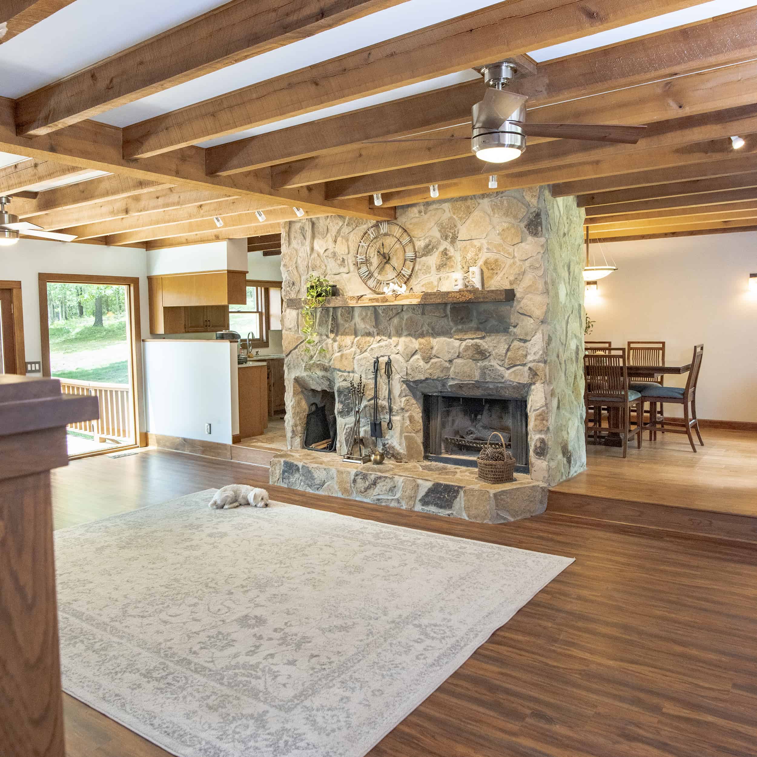 Rustic log cabin house with stone fireplace, wood beamed ceilings, and wood flooring in living room.
