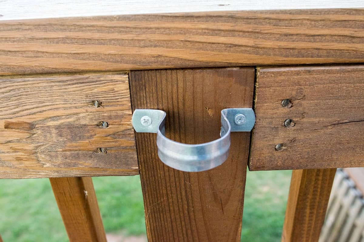 Pipe straps nailed to wooden deck posts to hang outdoor patio lights.