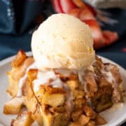 A slice of apple bread pudding with ice cream on top. Background of napkins and a small plate.