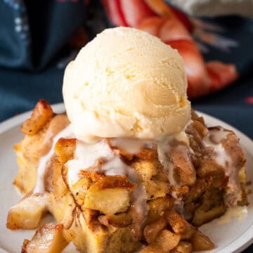 A slice of apple bread pudding with ice cream on top. Background of napkins and a small plate.