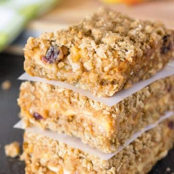 Apple crumb bars stacked three high with wax paper between them and an apple in the background.