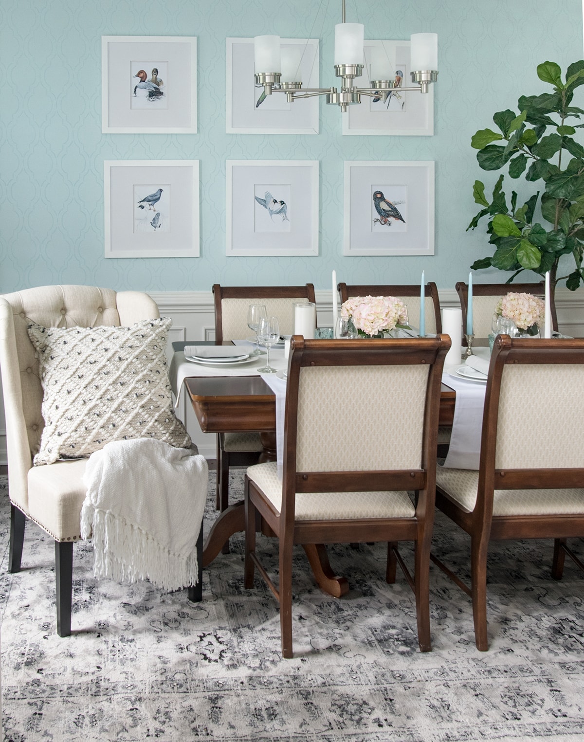 Classic chic dining room with area rug, natural accents, gray curtains, black lanterns, and soft blue walls.