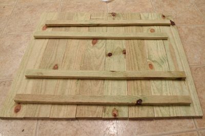 Back of natural wood pallet sign on beige tiled floor.