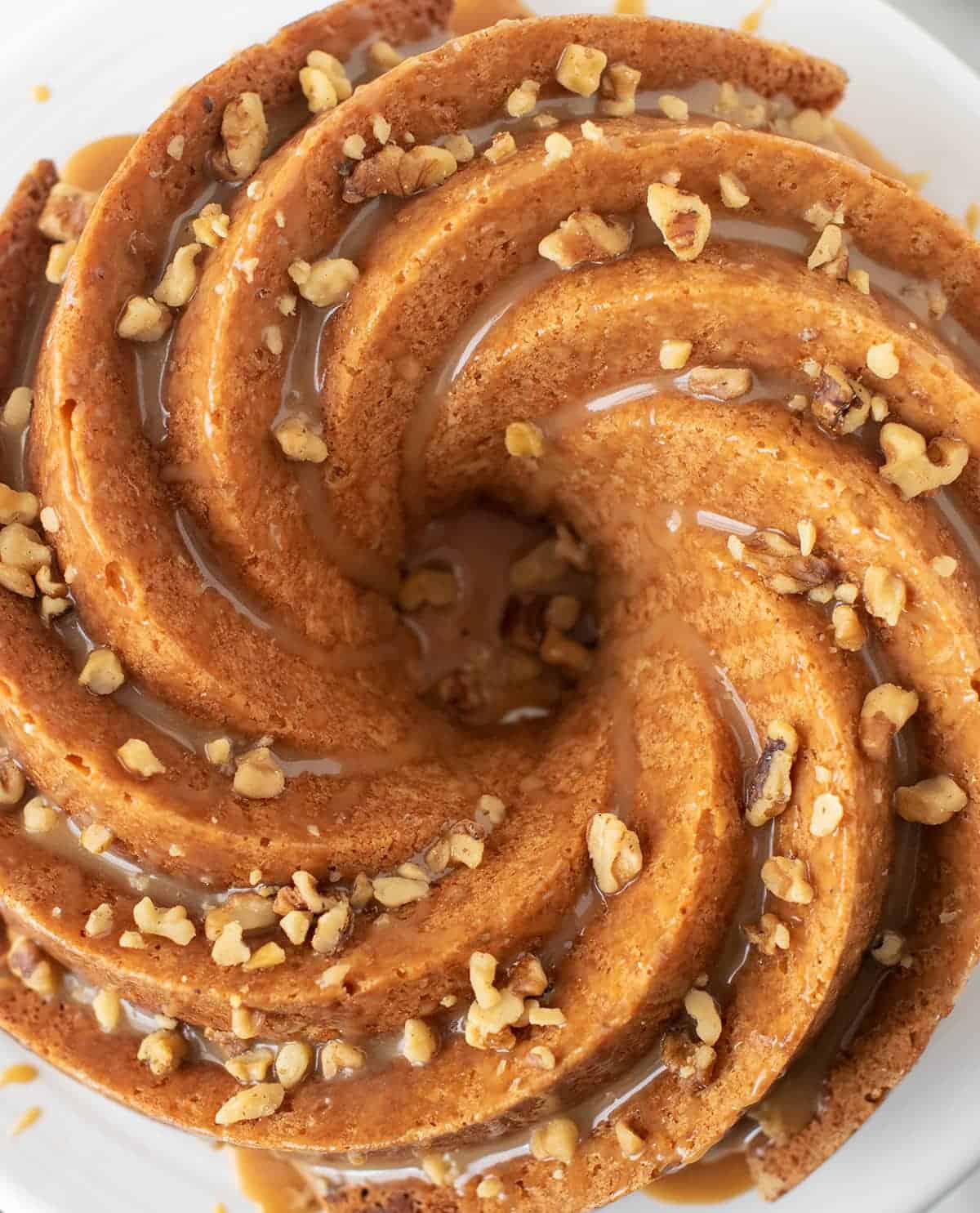 Aerial view of Bailey's Irish creme cake in a Beautiful bundt swirl pattern, topped with Bailey's caramel glaze and chopped walnut pieces.