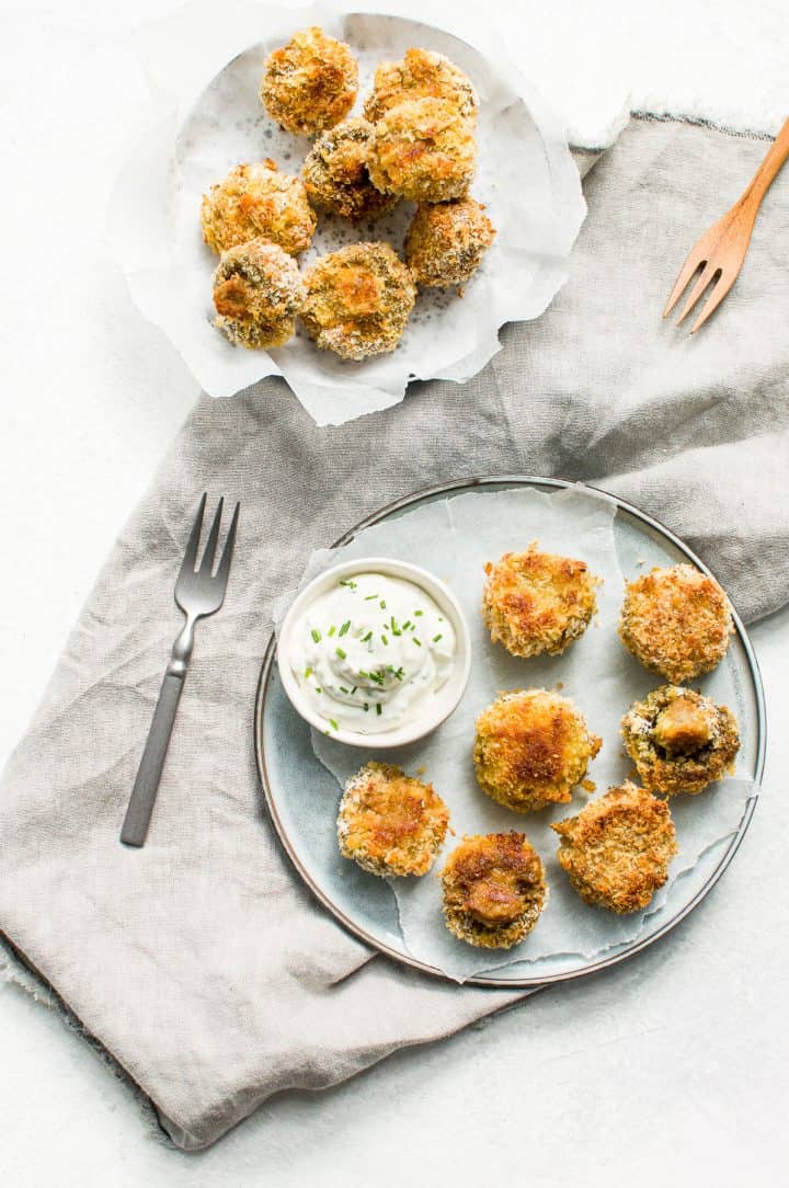 Breaded mushrooms on a plate with sour cream dipping sauce on the side.