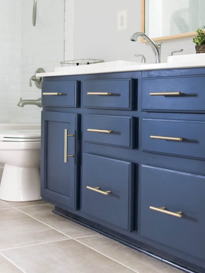 Midnight blue vanity with brass handles in a grey and white bathroom.
