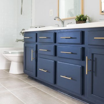 Midnight blue vanity with brass handles in a grey and white bathroom.
