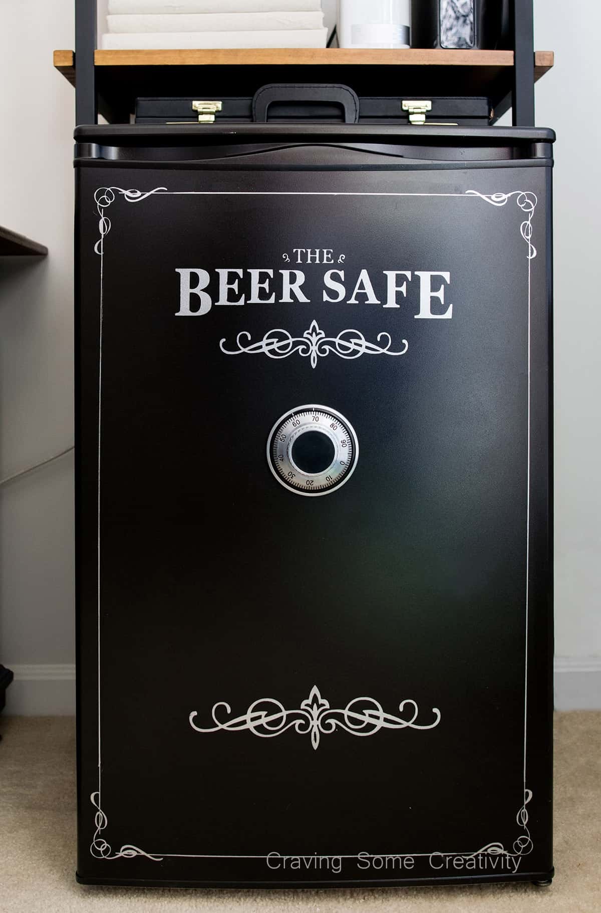 Black mini fridge with white beer safe stenciled detail and authentic safe dial on door.