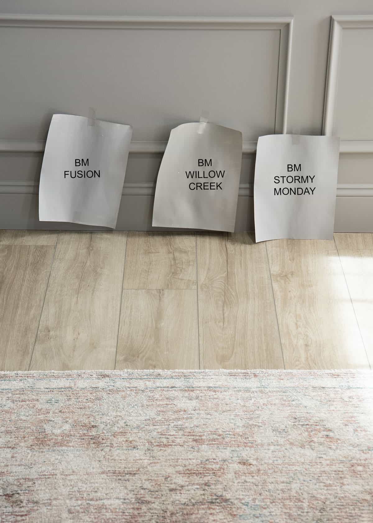 Samples of Benjamin Moore fusion, willow creek, and stormy Monday taped to the wall next to the floor.