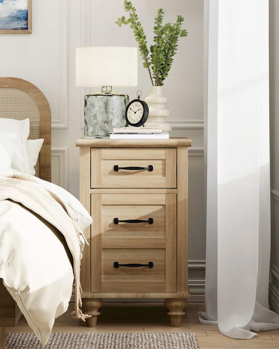Narrow light wood night stand with black handles in a bedroom.