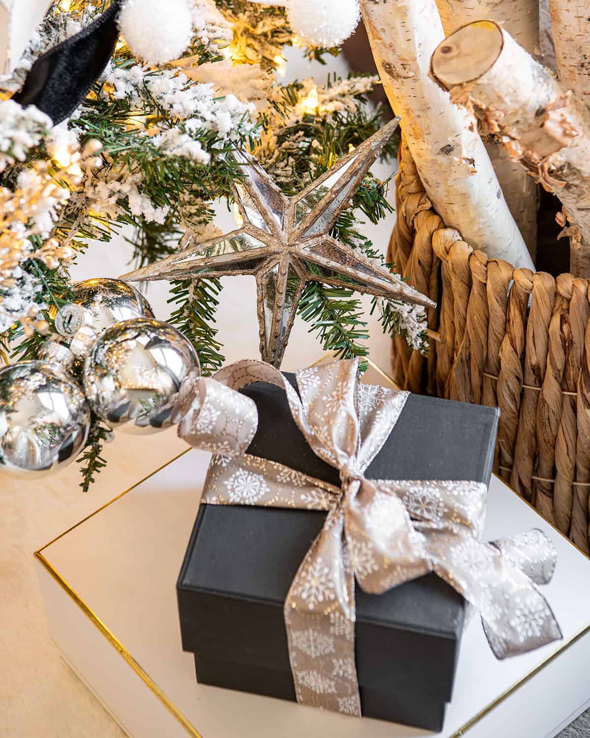 A black present box under a Christmas tree with birch logs and ornaments in the background.