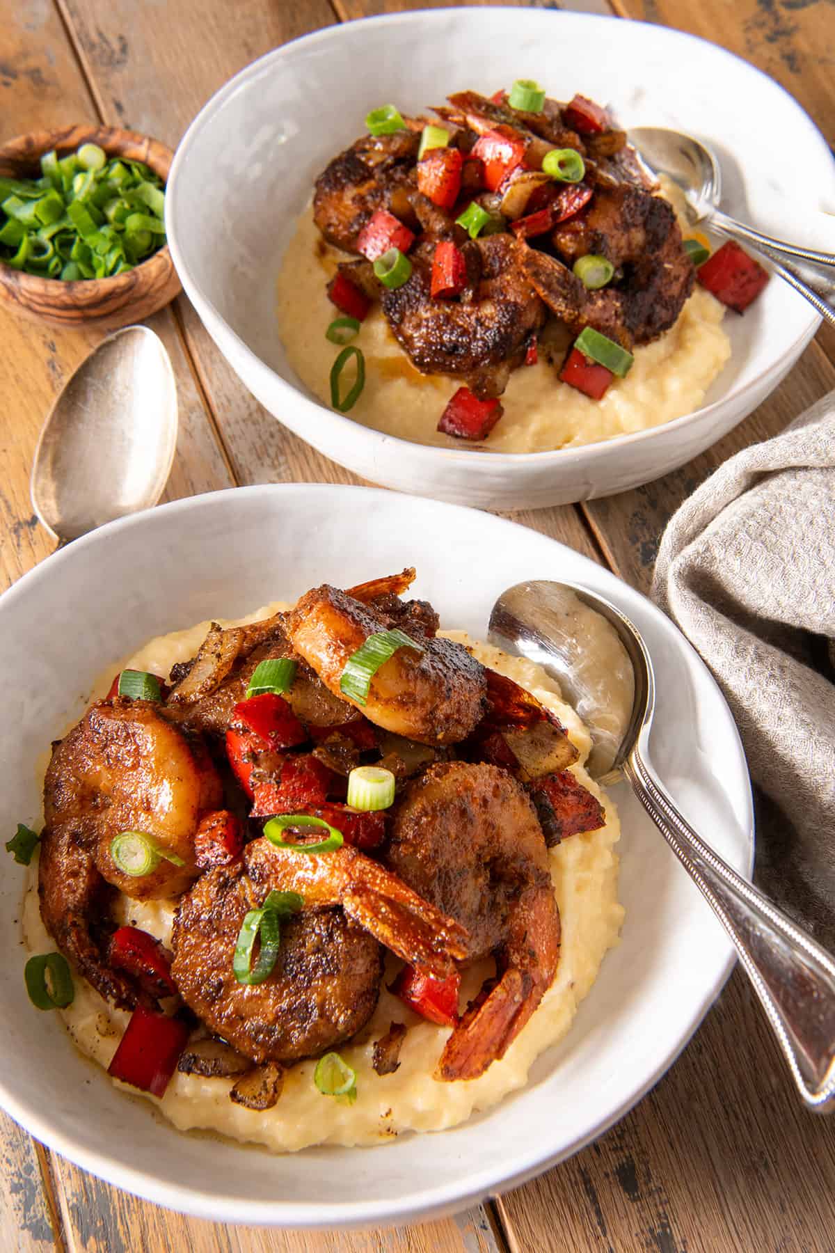 Two bowls of Cajun Shrimp and cheese grits topped with green onions and spoons.