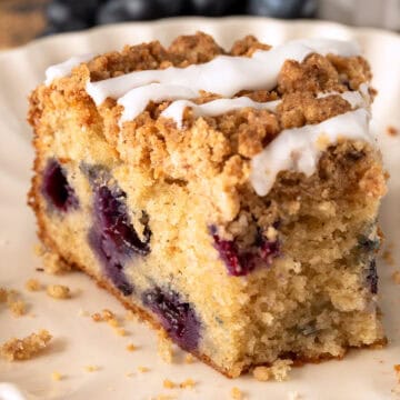 A slice of blueberry sour cream cake on a plate with a bite taken out.