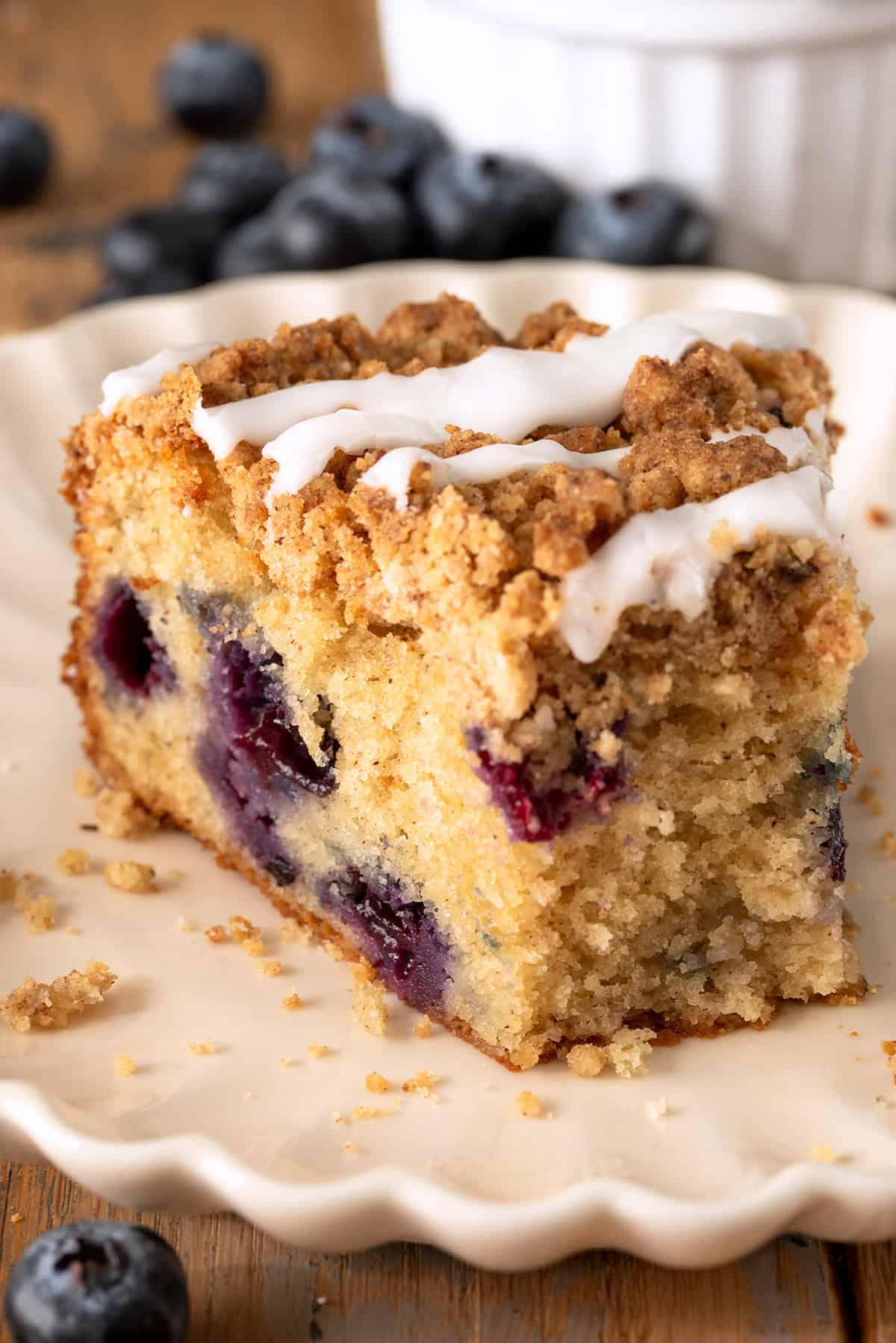 A slice of blueberry sour cream cake on a plate with a bite taken out.