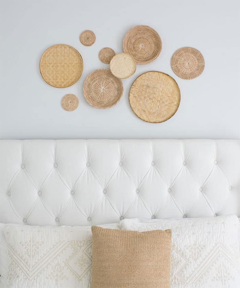 Woven rattan basket wall gallery above white plush headboard in bedroom.