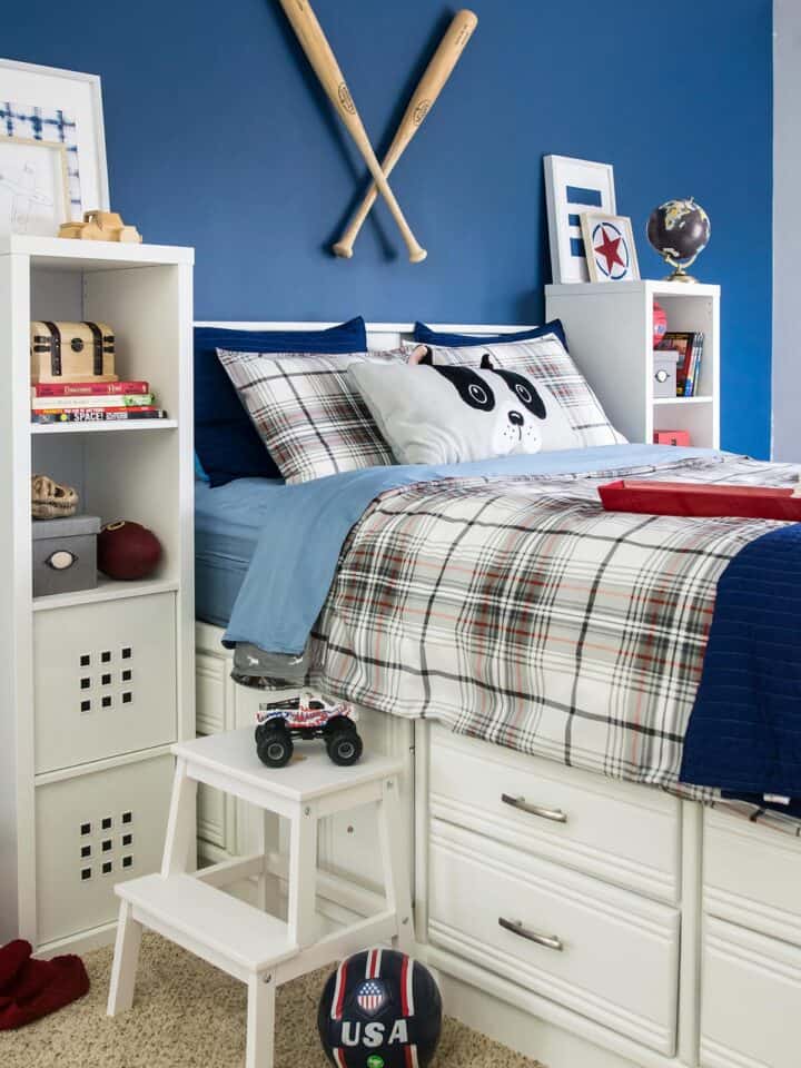 Blue boy's bedroom color scheme with white furniture, tall bed with drawers, blue wall, and baseball bats hanging as art.