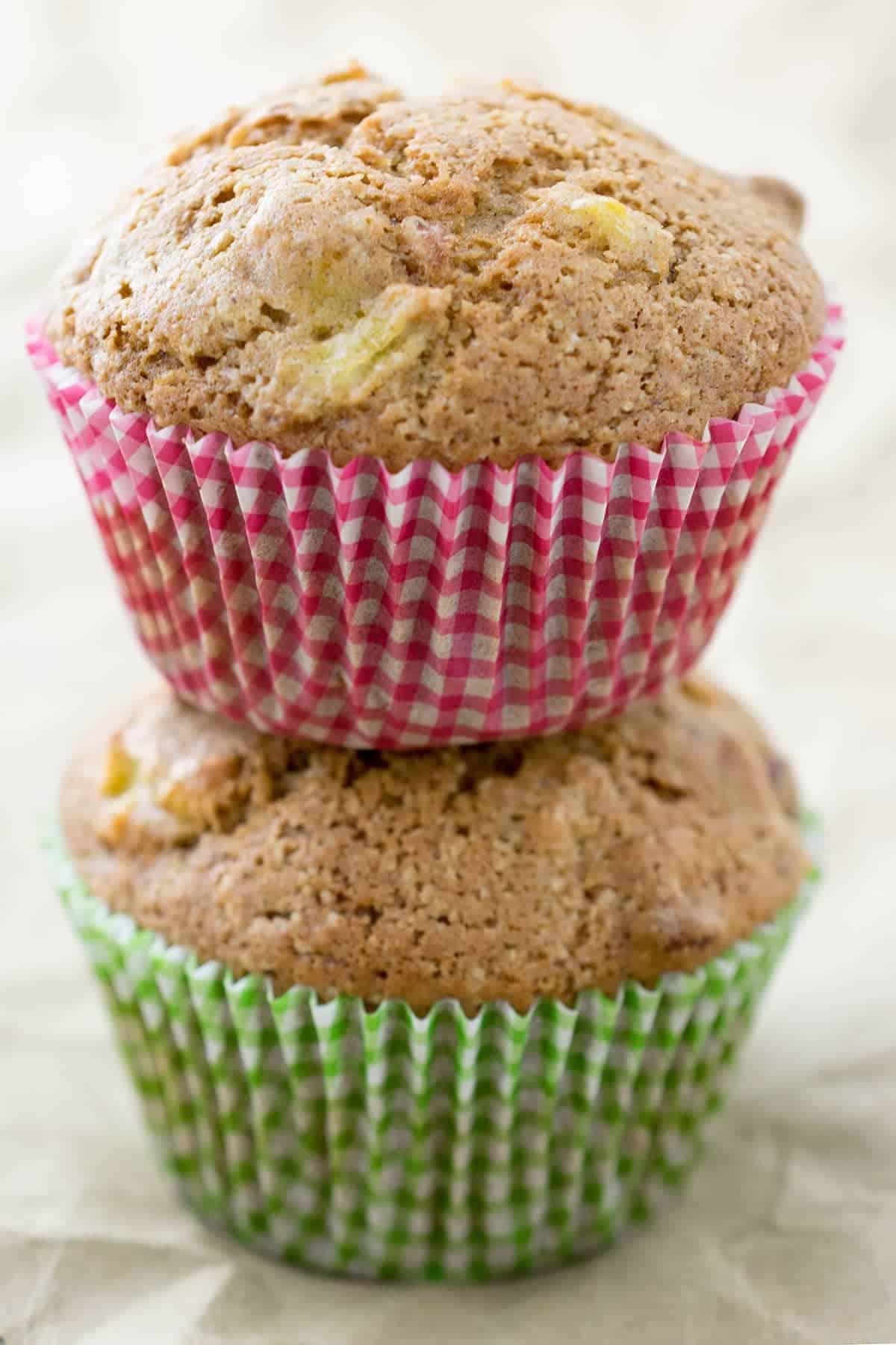 Two stacked summer squash muffins with red and green liners on top of crinkled paper surface.