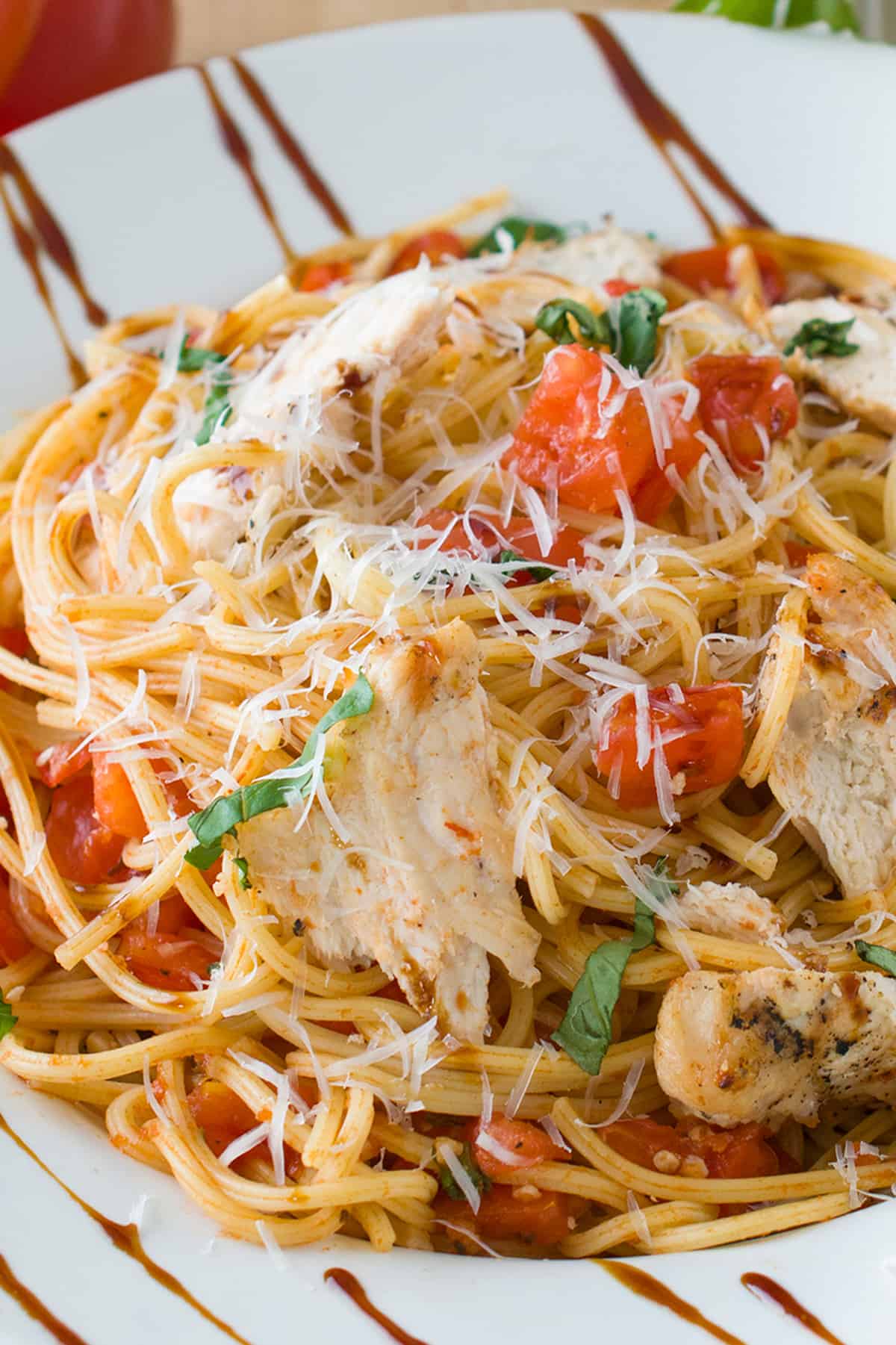 Bruschetta pasta with chicken in a rimmed bowl and topped with balsamic glaze.