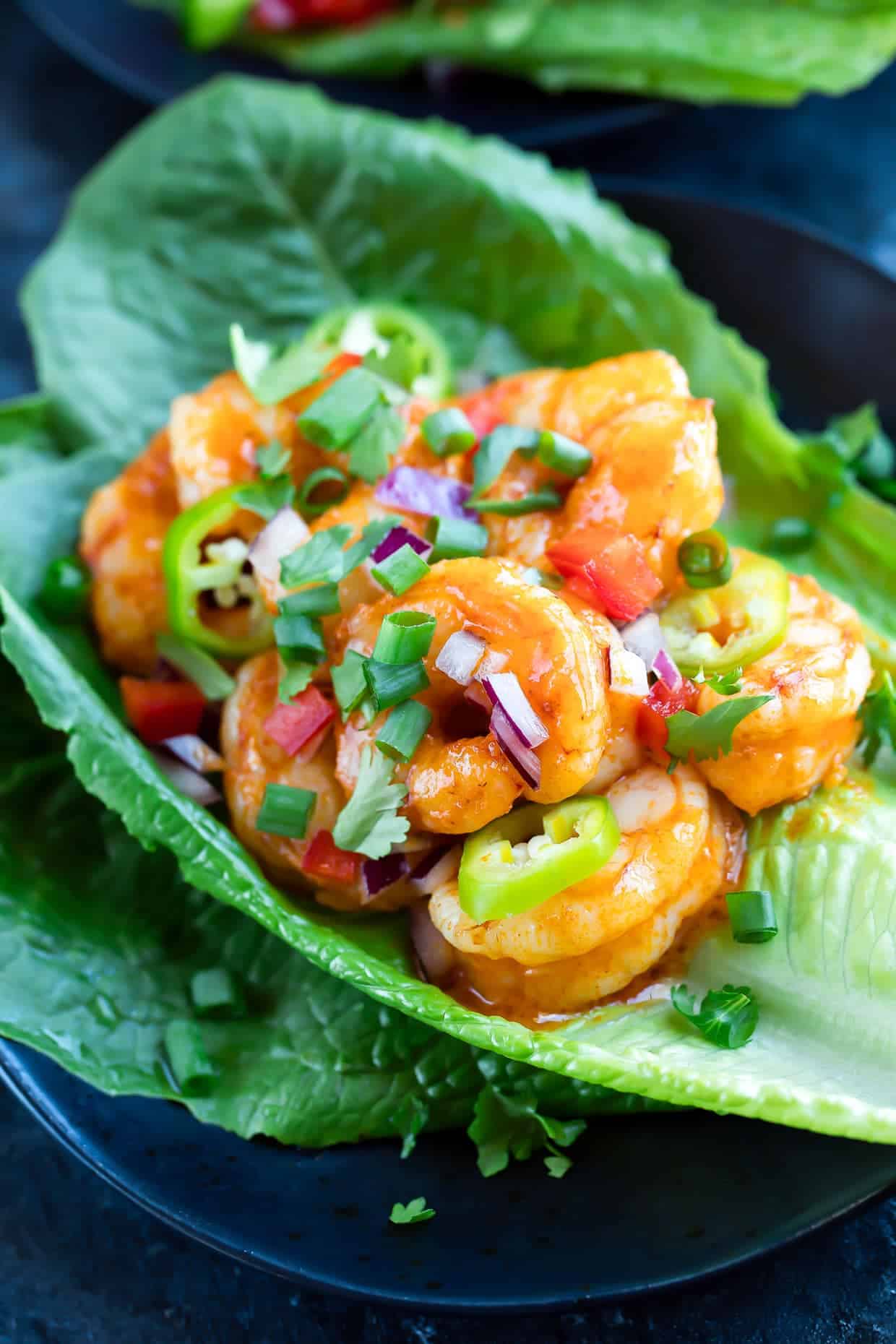 Buffalo Shrimp Lettuce Wraps with diced onion, tomato, and sliced jalapeno served on romaine lettuce.