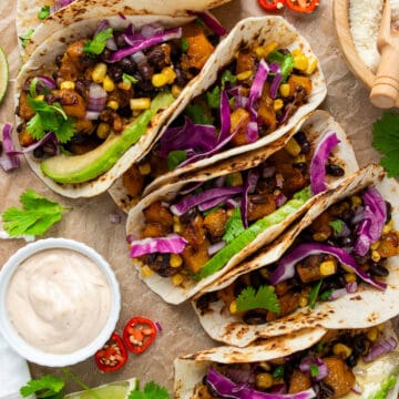 Overhead of several filled vegetarian tacos with cheese and sauces on the side.