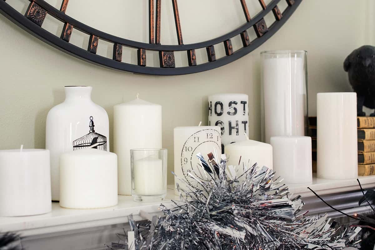 Halloween designed mantle with grouping of white candles, Edgar Allen Poe themed accessories, and stamped candles with black and white garland.