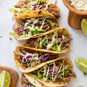 Carnitas Tacos with slaw and sauce sprinkled on top. Tacos are laid out on a white background.