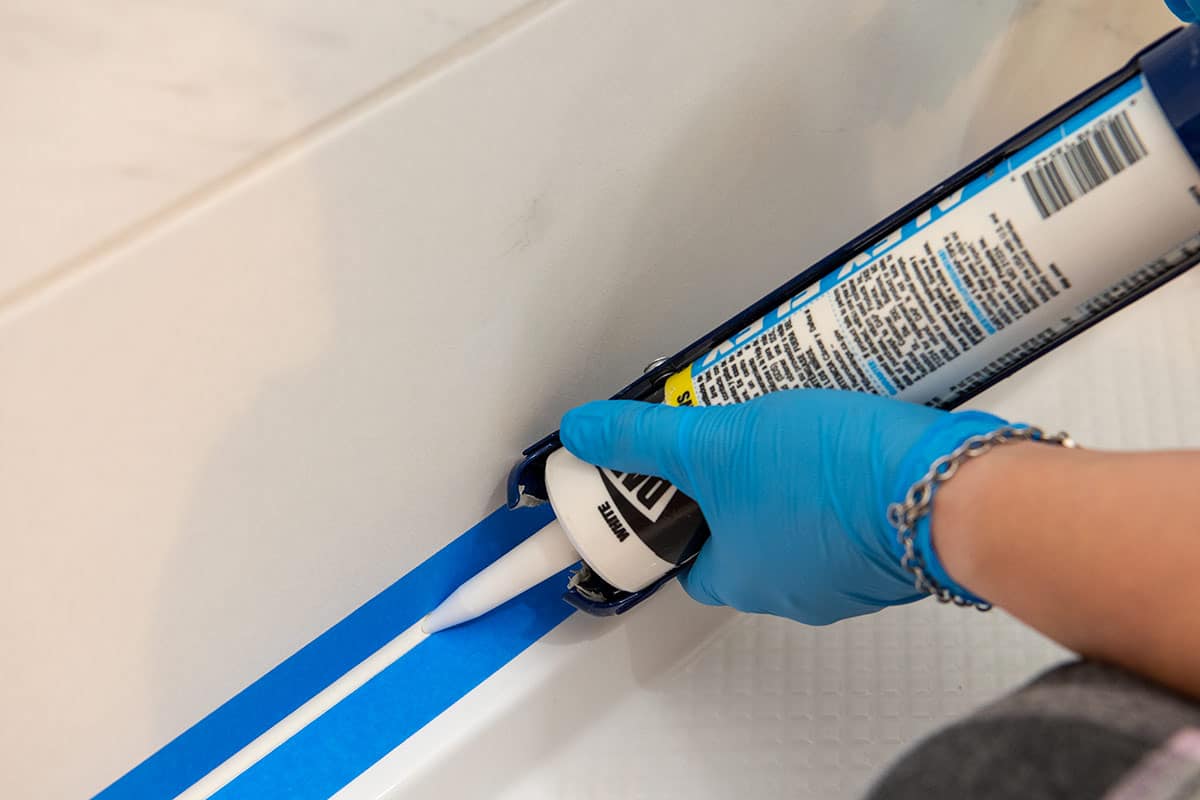 Woman running a bead of caulk down a shower pan.