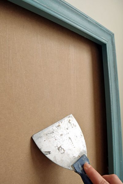 Scraping old adhesive from a cardboard background to prep it for painting.