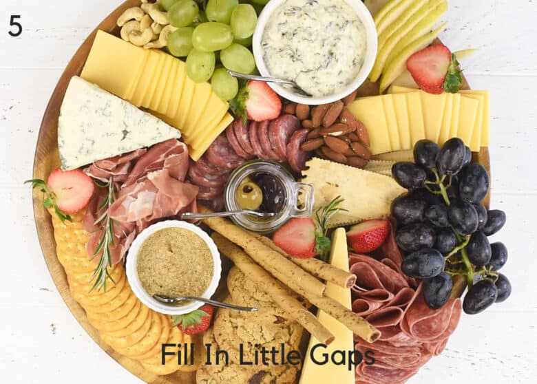 Top down of a filled charcuterie board featuring cured meats, cheeses, fruits, dip, and crackers.