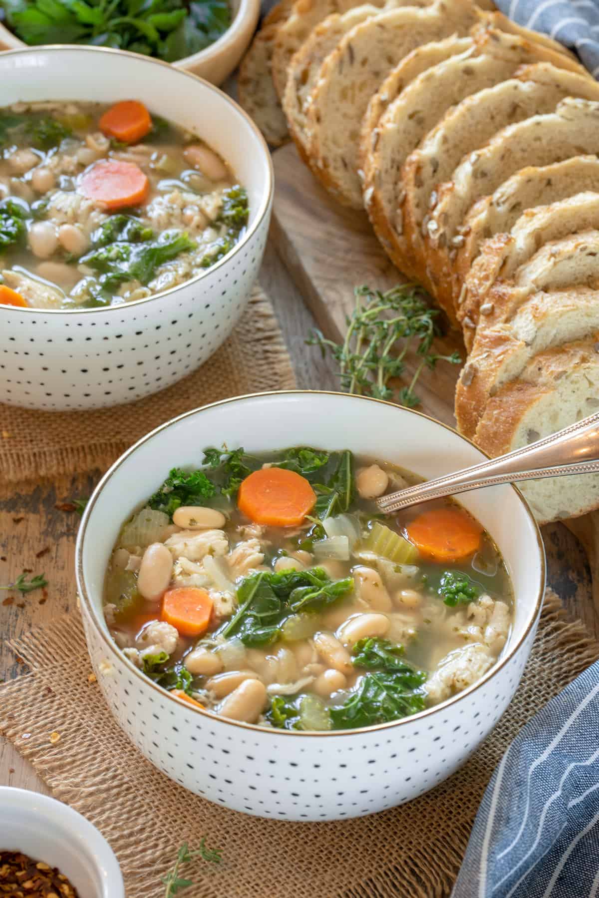 Bowl of chicken vegetable soup with carrots and beans and a spoon in the bowl.
