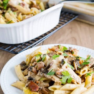Chicken marsala pasta on a white plate in front of a serving platter.