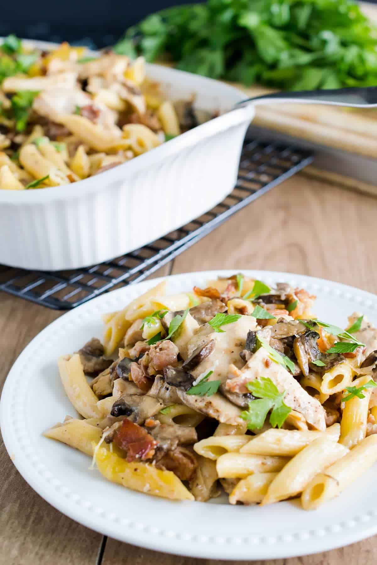 Chicken marsala pasta on a white plate in front of a serving platter.