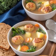 2 bowls of Chicken Meatball Soup with vegetables, carrots, and kale in a broth.