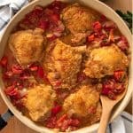 Top down shot of Chicken Cacciatore stewing in pan with tomatoes, spices, and diced onion while wood spoon stirs.
