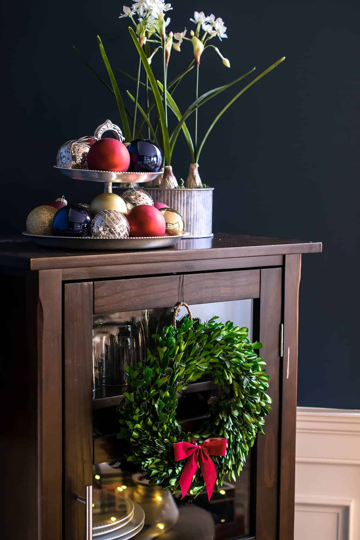 Christmas tiered tray on top of a small hutch in the din9ng room with boxwood wreath and paperwhites.