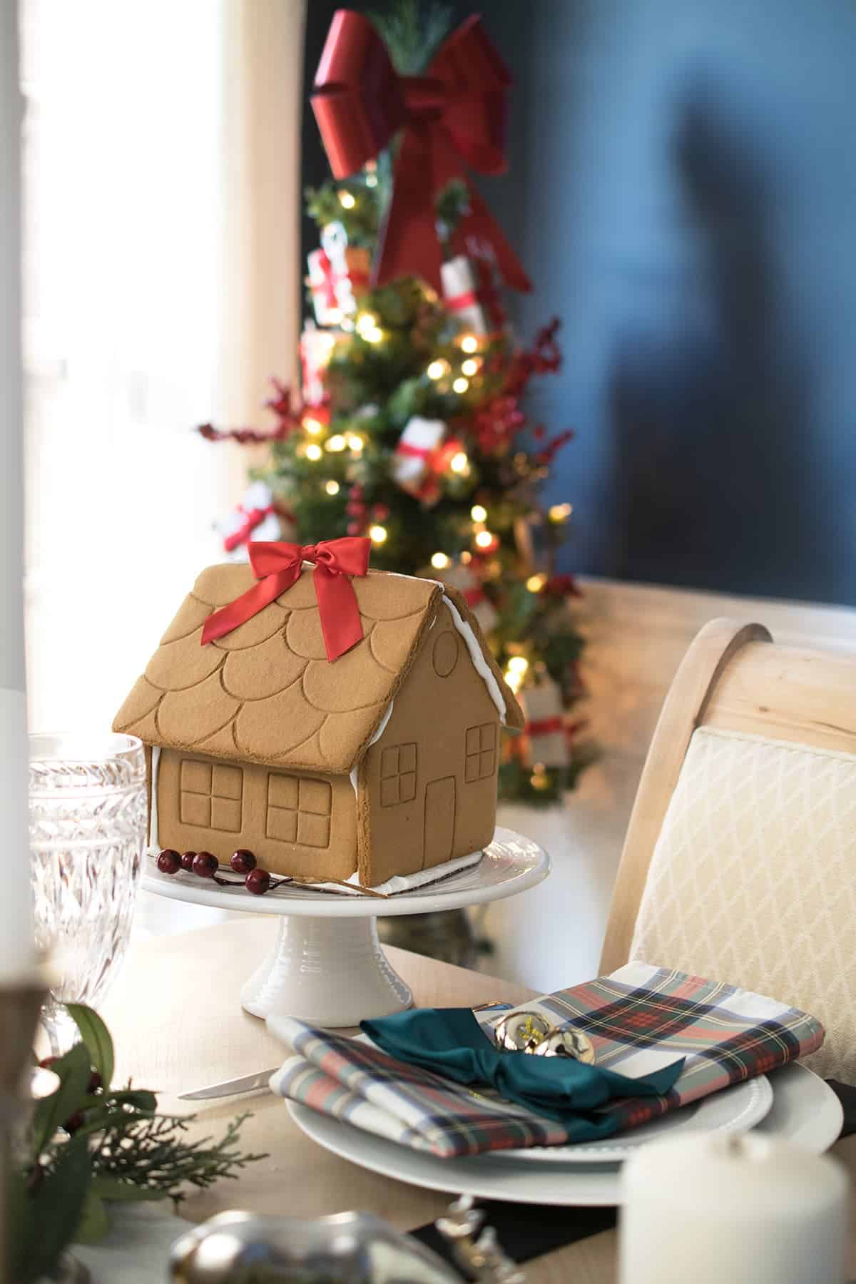 Christmas table decoration centerpiece with gingerbread house., crystal goblets, and tartan plaid napkins tied with green ribbon and a jingle bell.