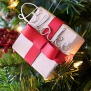Personalized DIY small gift boxes with red ribbon and and metal name tag hanging on Christmas tree.