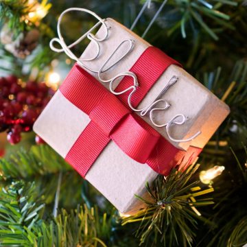 Personalized DIY small gift boxes with red ribbon and and metal name tag hanging on Christmas tree.