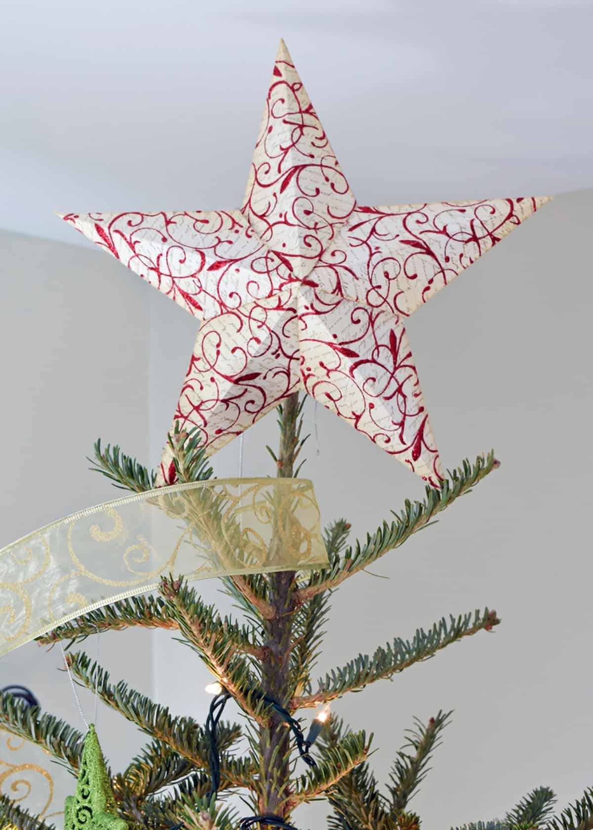 Red and white 3D paper star tree topper on top of Christmas tree with gold ribbon garland.