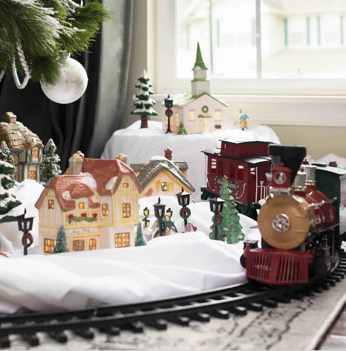 Train set under a tree with a small Christmas village on top of a white sheet.