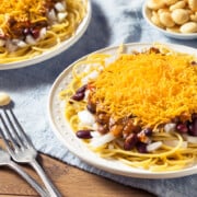 Cincinnati Chili on top of spaghetti noodles on two plates.