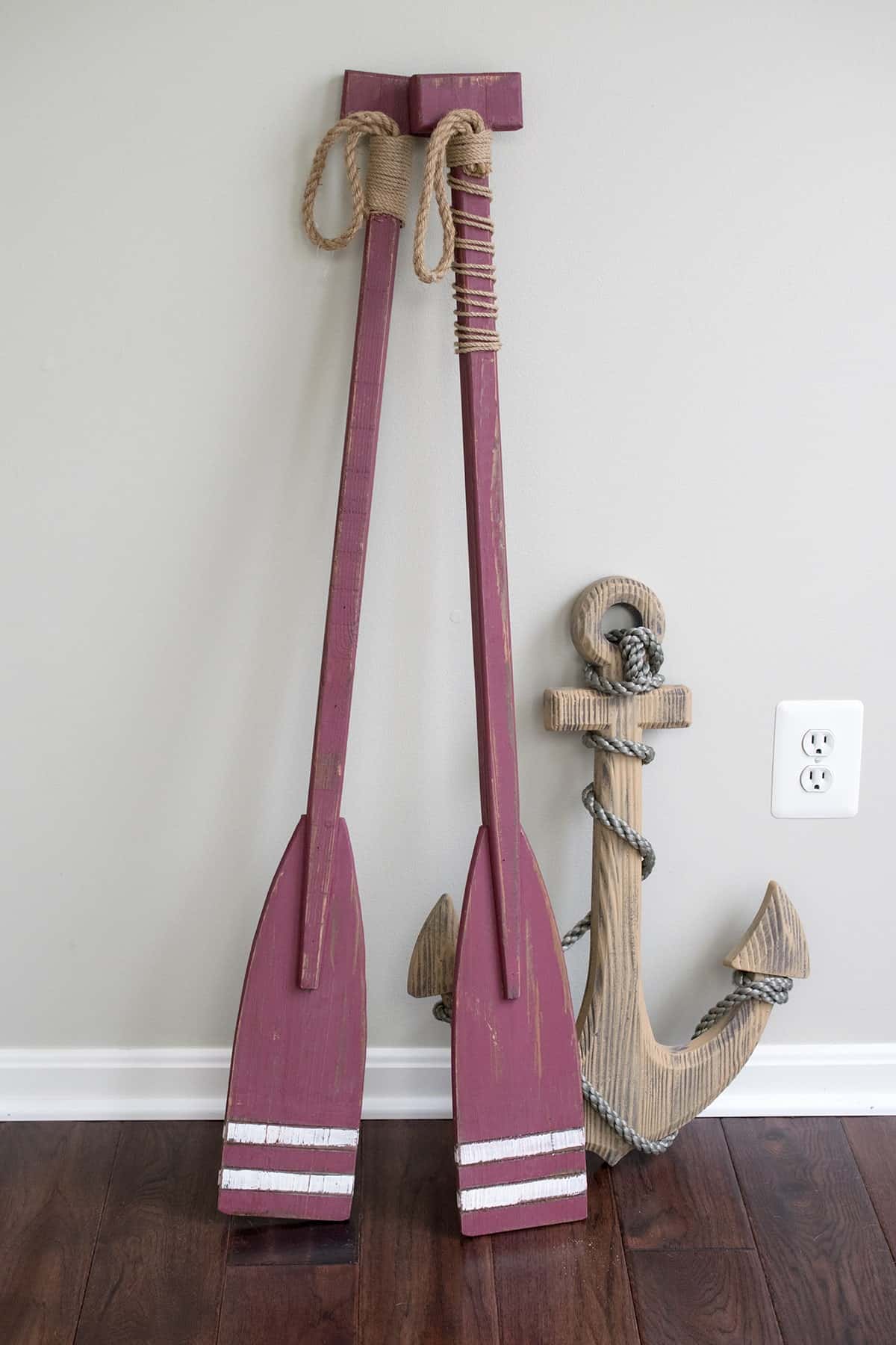 Maroon boating oars propped on soft gray wall before painting for budget friendly coastal decor.