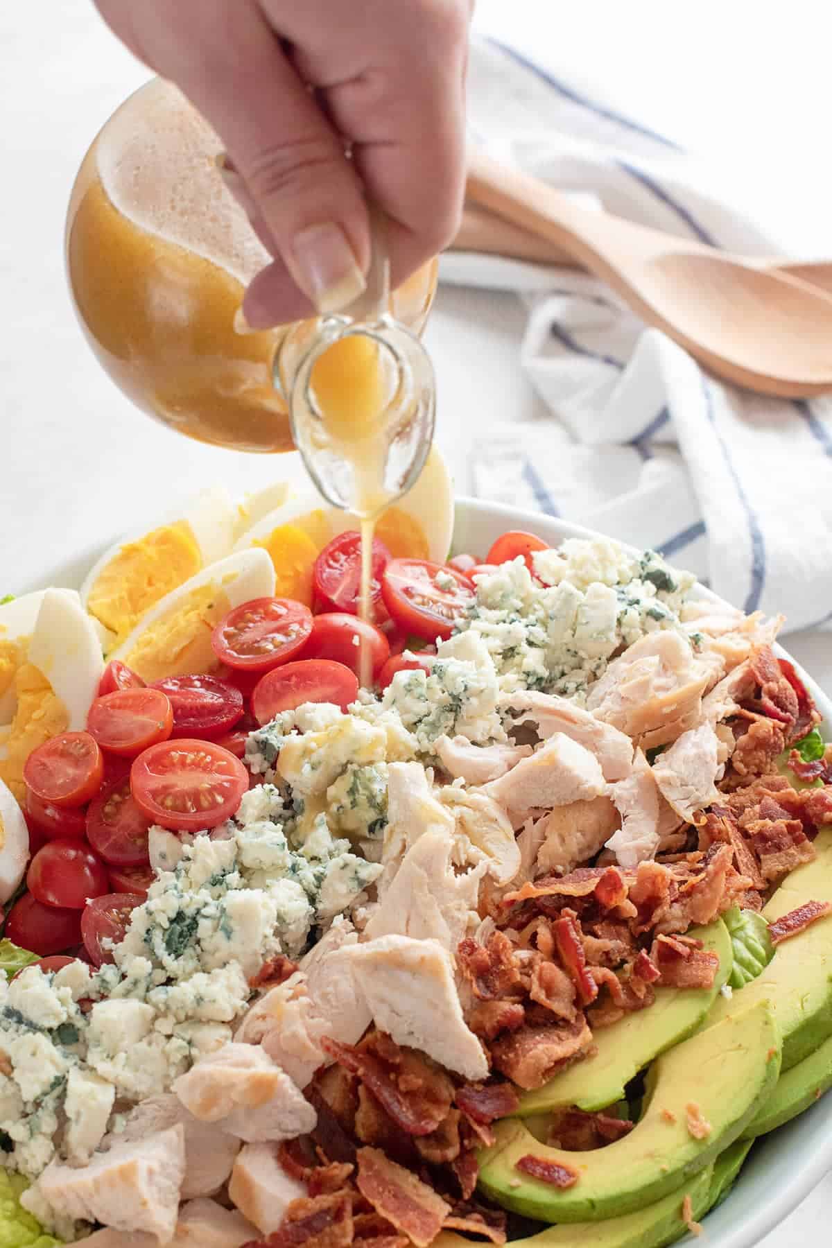 Cruet pouring white balsamic dressing over a cobb salad.