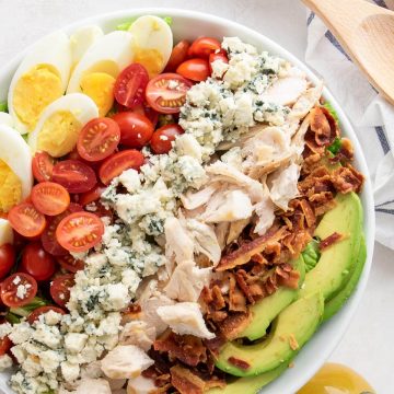 Cobb salad overhead with avocado, eggs, tomatoes, blue cheese crumbles, bacon, and chicken in a bowl.