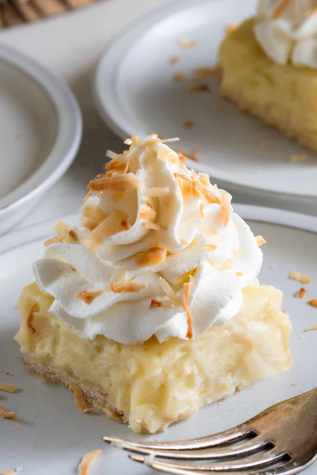 A slice of coconut cream pie bars on a plate with toasted coconut on top.