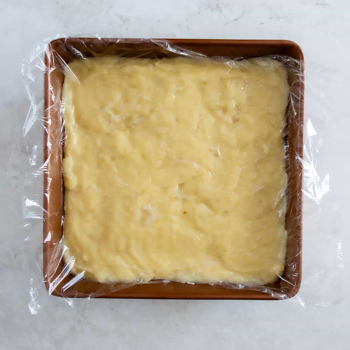 Coconut cream pie filling in a baking dish with plastic covering.