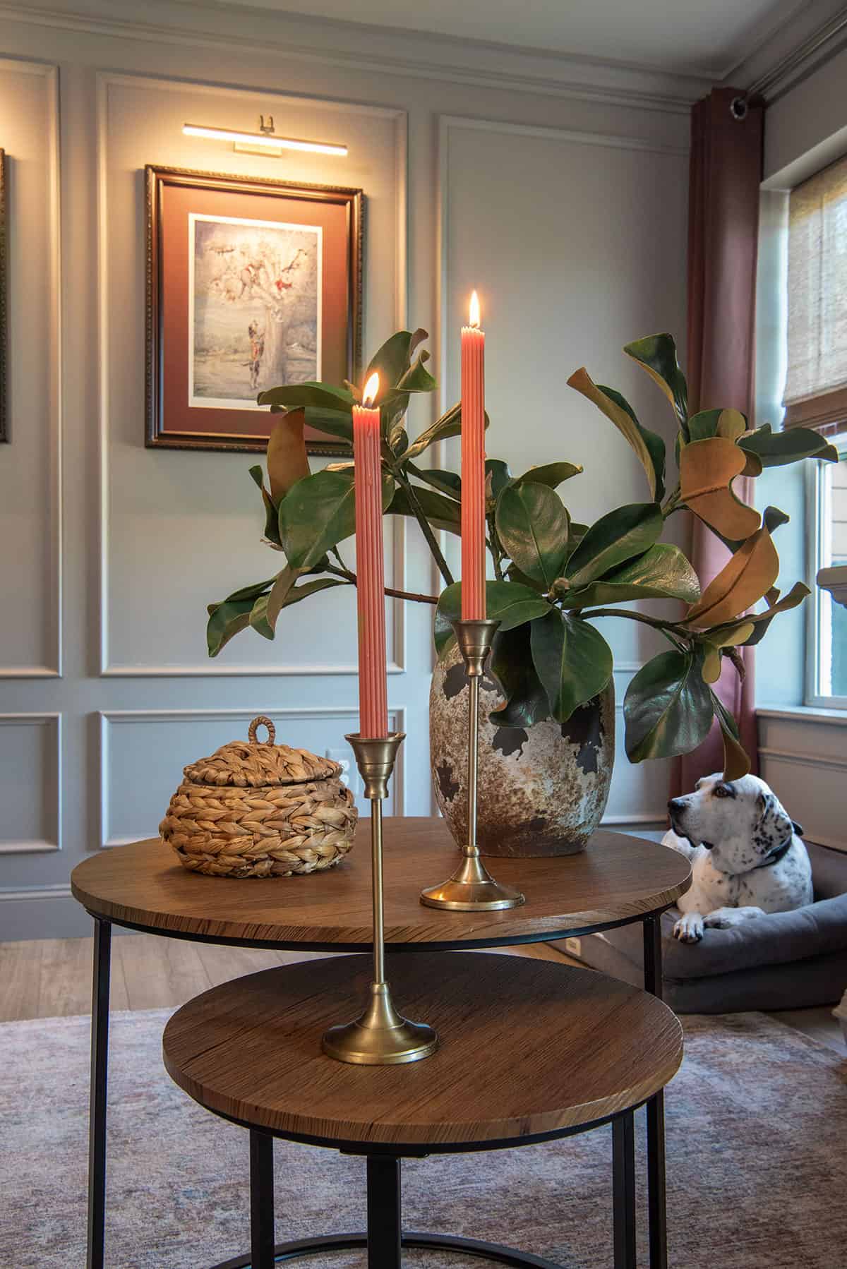 A living room with a nested wood coffee table with two candles and a magnolia plant on it.