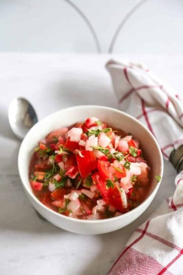 Cold vegetarian ceviche soup in a bowl with a napkin and spoon around it.
