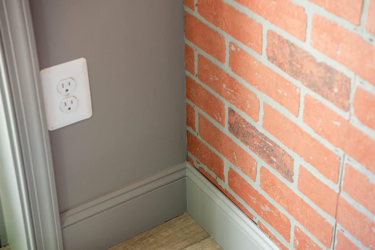 Corner of a room with a brick wall and baseboards.
